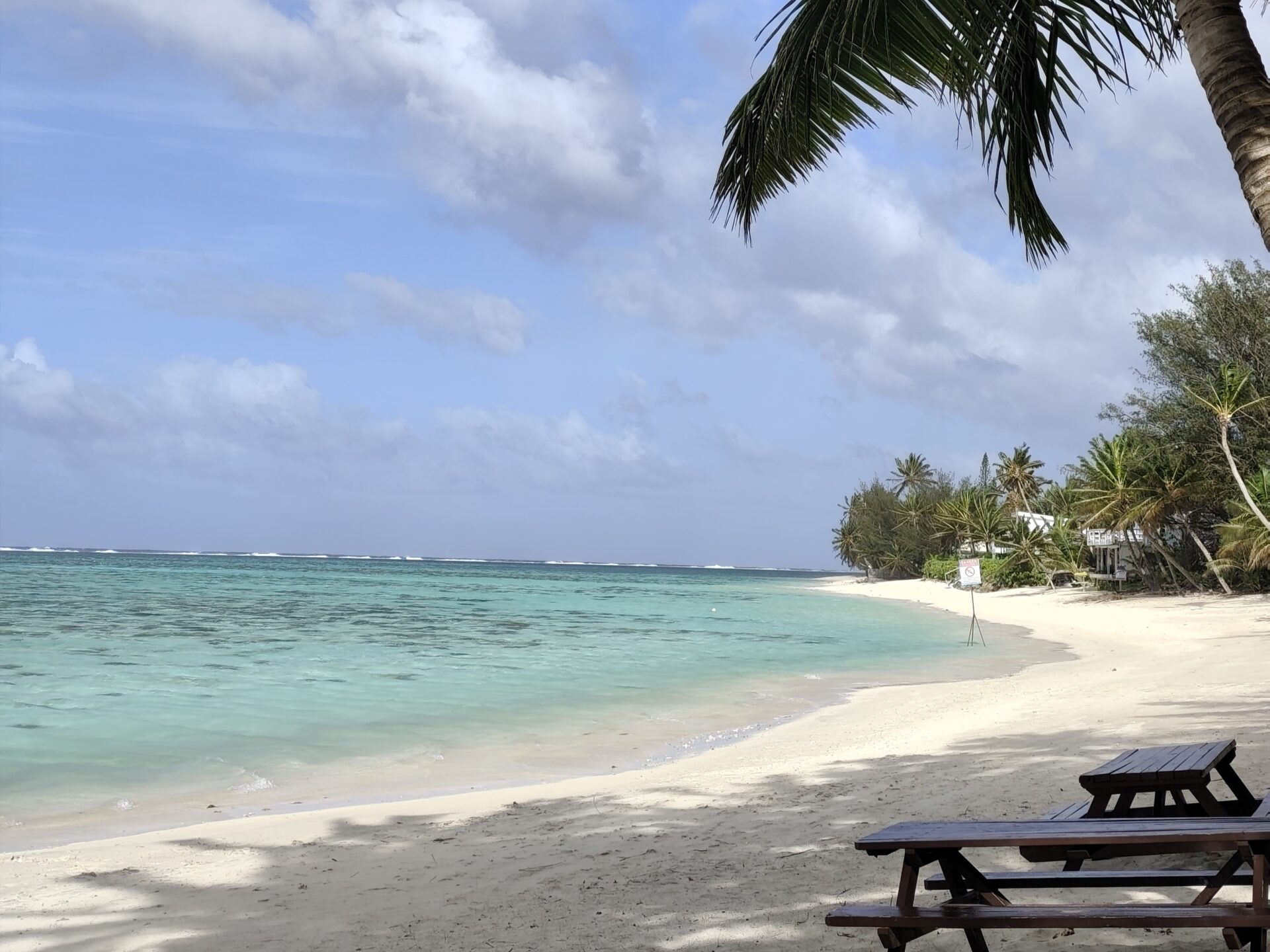 Idyllischer Aroa Beach auf Rarotonga mit weißem Sandstrand, Palmen, türkisfarbenem Lagunenwasser und sonnigem Himmel – Top-Spot für Schnorcheln und Sonnenuntergänge auf den Cookinseln.