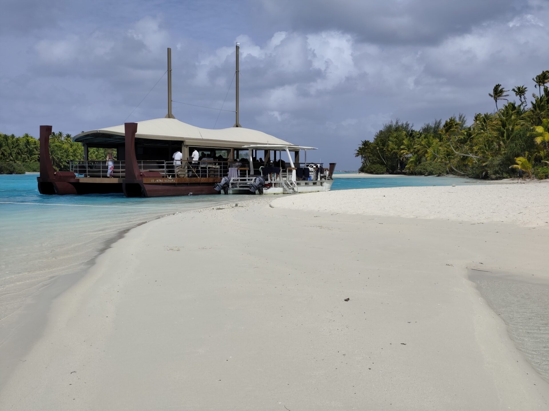Traditionelles Auslegerkanu (Vaka) in der flachen, türkisen Aitutaki-Lagune mit weißem Sandstrand und unbewohnten Motus.