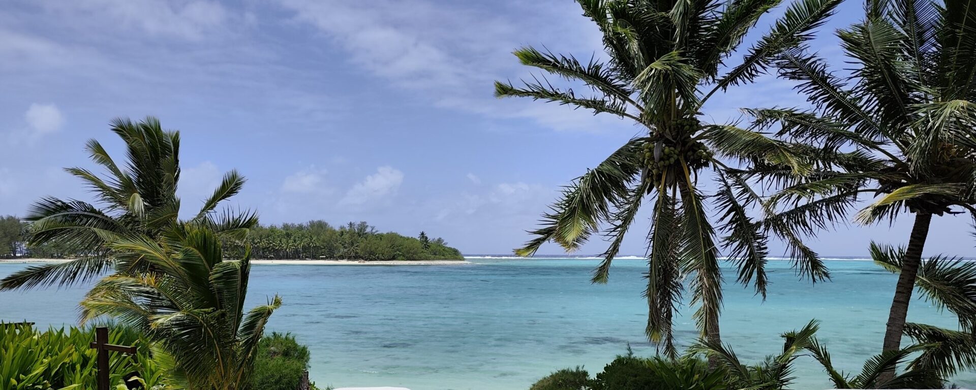Panoramablick auf Cookinseln-Paradies mit Palmen, weißem Sandstrand, türkisfarbenem Lagunenwasser und ferner Insel – typisches Südsee-Idyll!